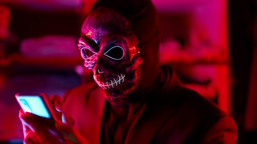 a Man in a Scary Glowing Death Mask Holds a Phone in Hands and Pokes Finger at the Screen in a Neon