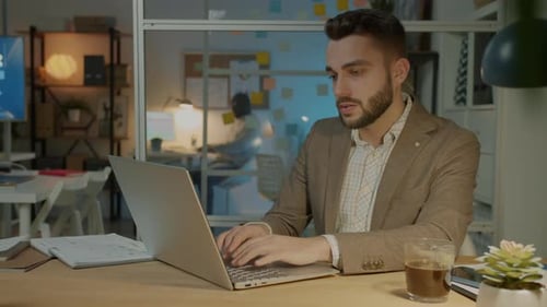 Young Businessman Using Computer in Dark Office Concentrated on Work