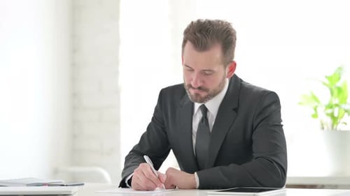 Young Businessman Writing on Paper in Office