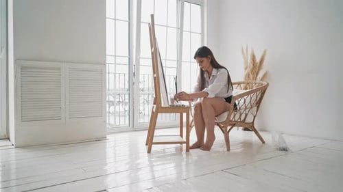Barefoot Woman Works with Paints on Wooden Easel in Studio
