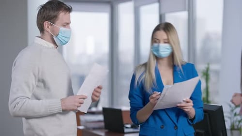 Coworkers Discussing Paperwork Wearing Masks in Office