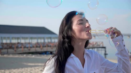 Pretty Woman Blowing Soap Bubbles on the Beach with a Sea on Background Slow Motion