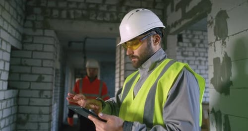 Male Engineer Browsing Tablet and Consulting Colleague on Construction Site
