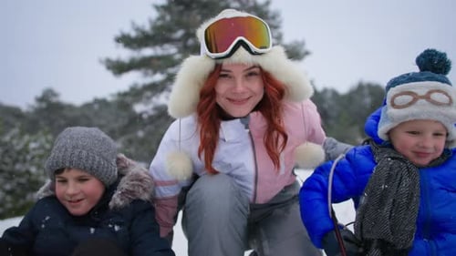 Happy Winter Holidays in Forest Outdoors Closeup Mom Looks at the Camera Then Helps Her Sons on a