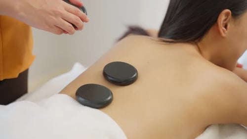 Asiatische junge entspannende Frau bekommt Rückenmassage mit heißem Stein