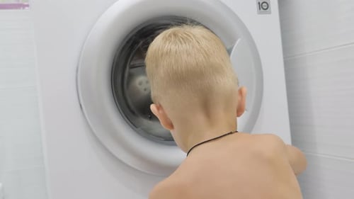 Ein süßer Junge beobachtet zu Hause die Waschmaschine.
