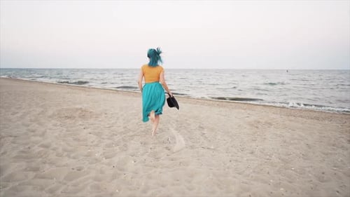 Hübsche Frau mit gefärbten blauen Haaren läuft in der Nähe von Meer oder Meer und genießt die Freiheit in den Sommerferien