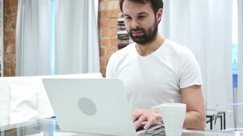 Bartmann trinkt Kaffee aus der Tasse und arbeitet am Laptop