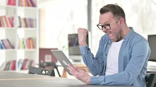 Excited Man Celebrating While Using a Tablet Indoors