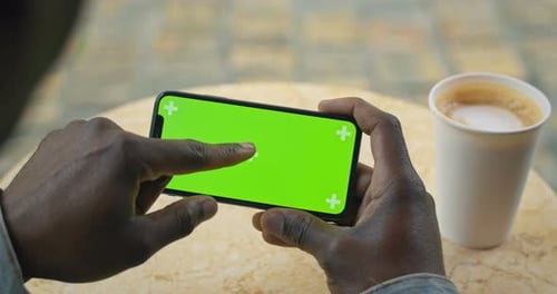 Hands of Afro American Man Sits at Table with Paper Coffee Cup on It Holding Smartphone Horizontal