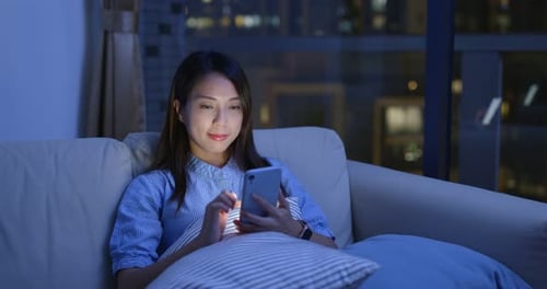 Woman Using Smartphone on Sofa at Night