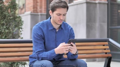 Man Using Smartphone While Sitting on Park Bench