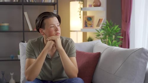 Young Adult Sitting, Lost in Thought on Sofa