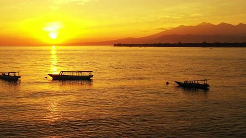 Silhouette of boats floating on calm sea surface under golden sunset with yellow sun setting down th