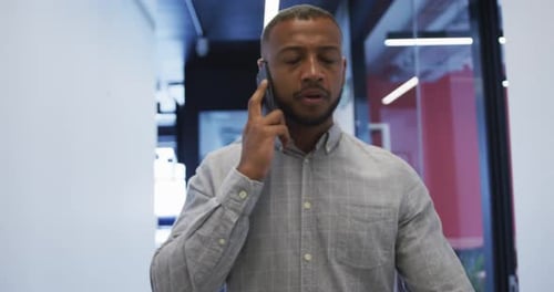 Mixed race businessman walking talking on smartphone checking his watch in modern office