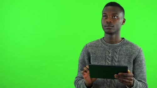 A Young Black Man Works on a Tablet with a Smile - Green Screen Studio