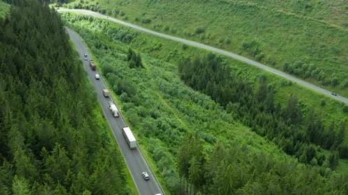 Luftaufnahme der Straße mit fahrenden Autos und Lastwagen in den Bergen mit hoher grüner Tannenblattkiefer