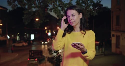 Woman in Yellow Sweater Using Her Smartphone Among the Colourful Lights of Night City