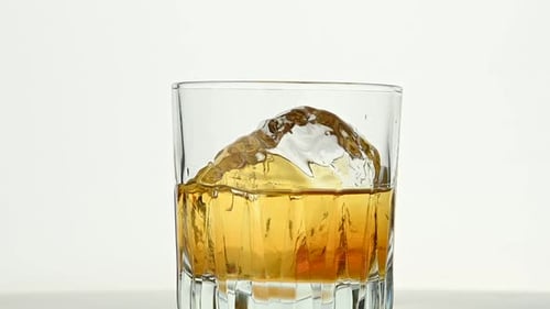 Ein großer Eisfelsen dreht sich im Whiskyglas auf Weiß