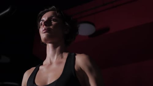 Female Bodybuilder Lifting Weights in a Dark Gym