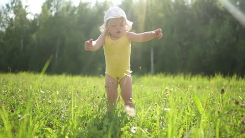 Little Funny Cute Blonde Girl Child Toddler in Yellow Bodysuit and White Hat Walking in Field with