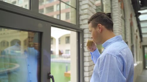 Man Drinking Coffee by Window in Urban Setting