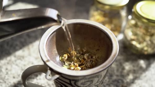 Pouring hot water into a cup to prepare tea with medicinal herbs. Close-up slow motion.