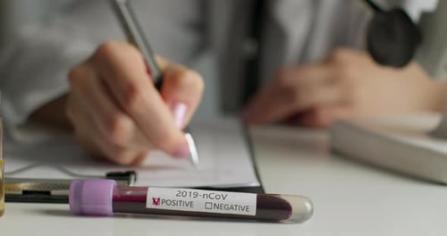 Close-up Shot. The Doctor Is Filling Out the Documents. In the Foreground Are Test Tubes with a Test