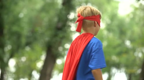 Boy Wearing Superhero Costume Flexes Muscles Outside