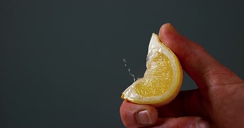 Hand Squeezing Lemon Wedge Causing Juice to Spray