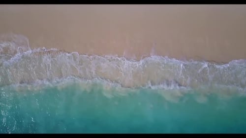 Aerial drone shot landscape of idyllic shore beach vacation by blue green sea with bright sand backg