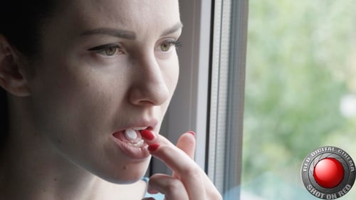 Woman taking pill and drinking water by window
