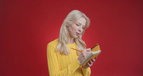 Woman Writes in Notepad on Red Background