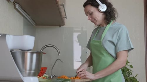 Woman Chopping Carrots in Kitchen with Headphones