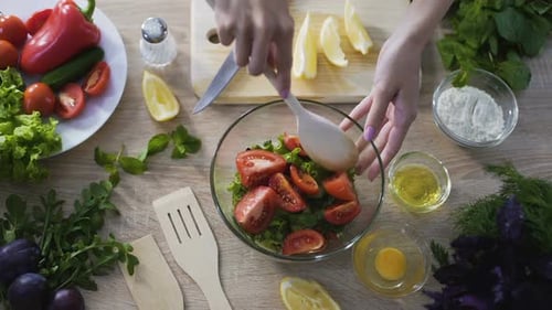 Top view of female hands mixing freshly cooked salad and showing it into camera