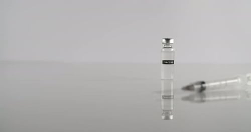 Vaccine Vial with Needle on Reflective Surface