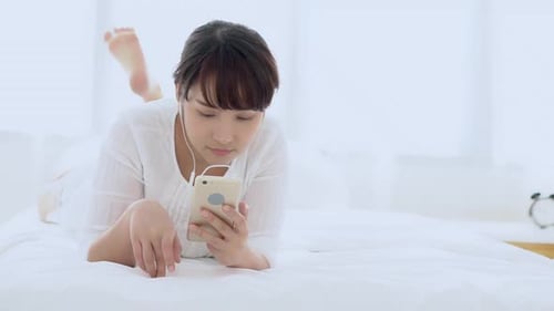 Woman Using Smartphone Lying on Bed Indoors