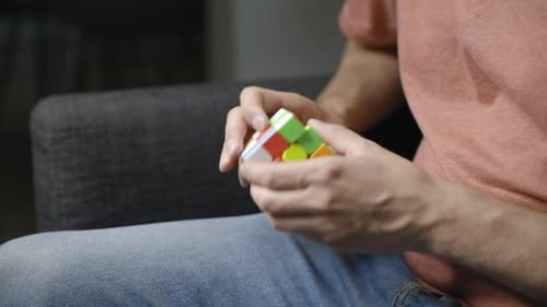 Mãos masculinas jovens giram e torcem os lados do cubo de Rubik, visto de lado