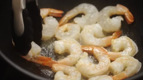 Delicious Shrimp Sizzling in Pan being Moved with Tongs