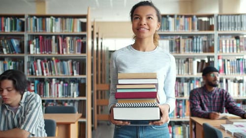 Pretty Mixed Race Lady Student Carrying Books Walking in Library Smiling