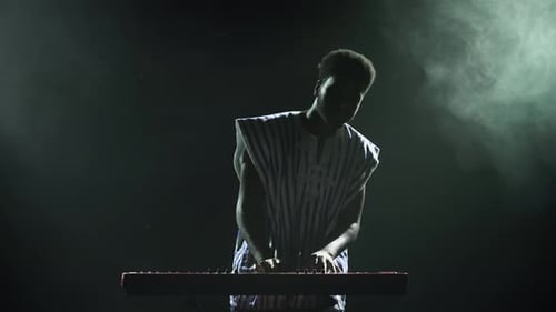 Silhouette of African American Man Playing Piano Synthesizer on Stage in Dark Smoky Studio