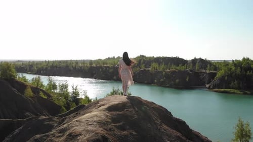 Woman Stands Atop Hill Overlooking Turquoise Lake