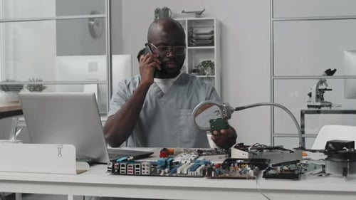 Black Engineer Talking on Phone and Examining Chip