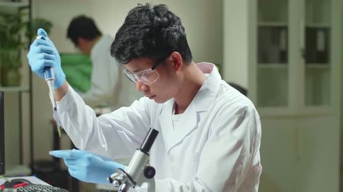 Asiatischer Wissenschaftler entnimmt genetische Lösung aus dem Reagenzglas mit Mikropipette und steckt sie in eine Petrischale