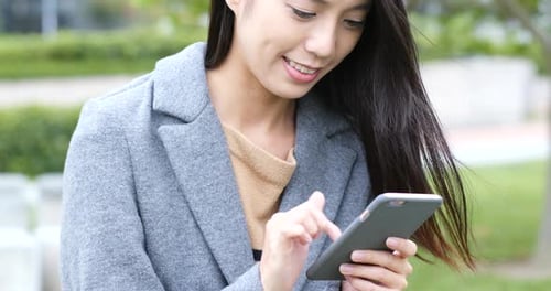 Woman Using Smartphone in Park with a Smile