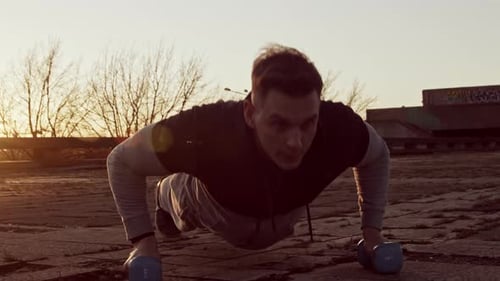 Man Doing Pushups with Dumbbells at Sunset
