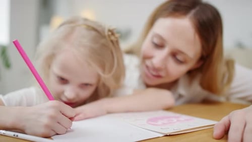 Child Writing in Notebook Beside Smiling Adult