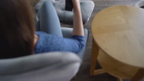 Woman is Sitting in a Chair Watching TV with a Green Screen Switching Channels with a Remote Control