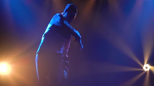 Silhouettes of a Young Guy Practicing Breakdancing in a Dark Studio in the Spotlight. Close Up. Slow