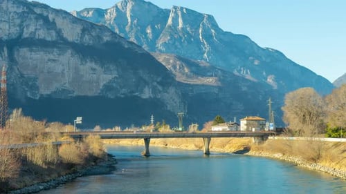 Cars Drive on Bridge Over River Against Rocky Mountains